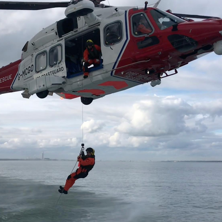 Two men hanging from a helicopter above the sea